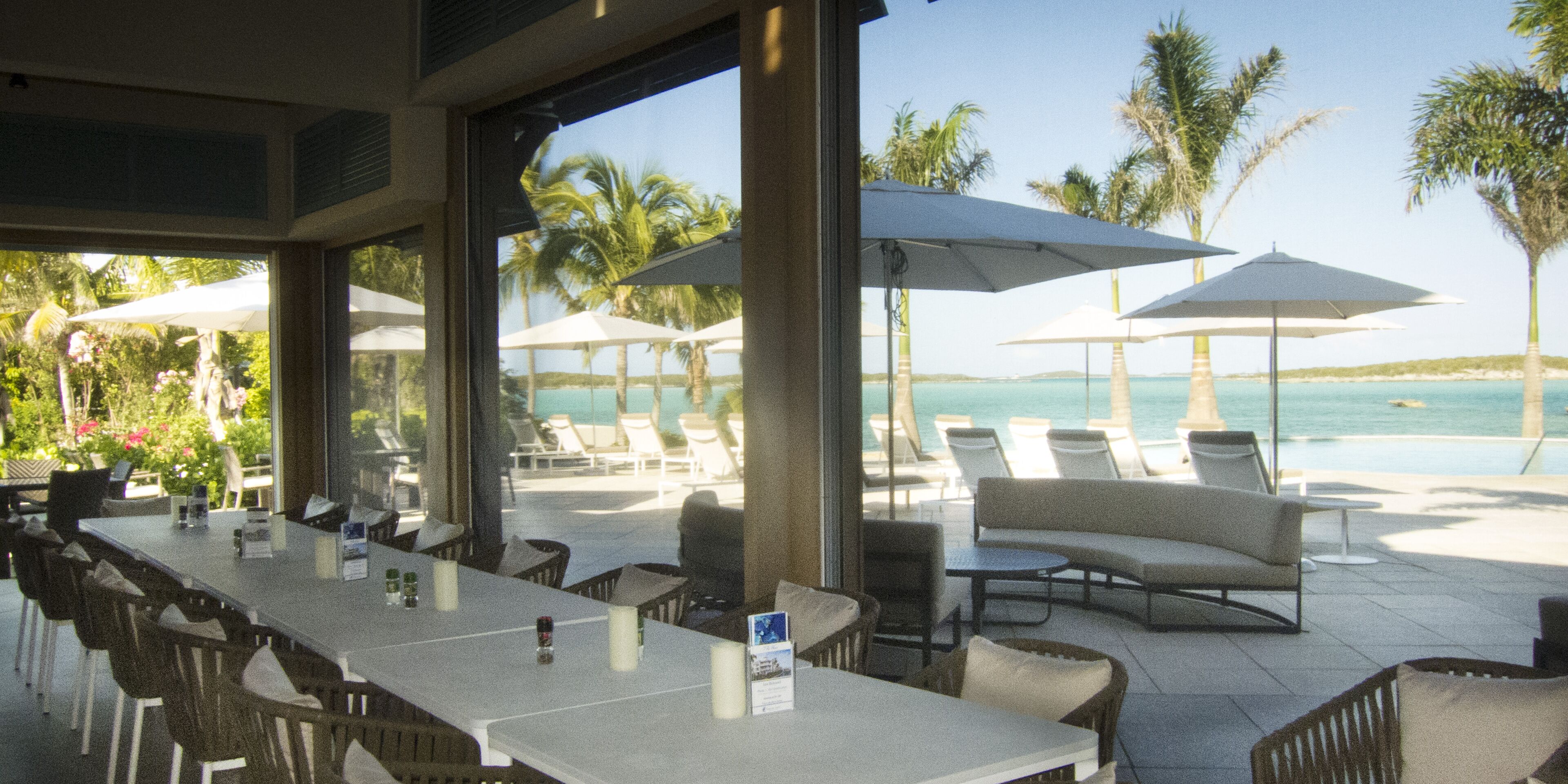 Un espace extérieur aménagé pour les repas, avec des tables et des chaises, offrant une vue sur une piscine et des palmiers.