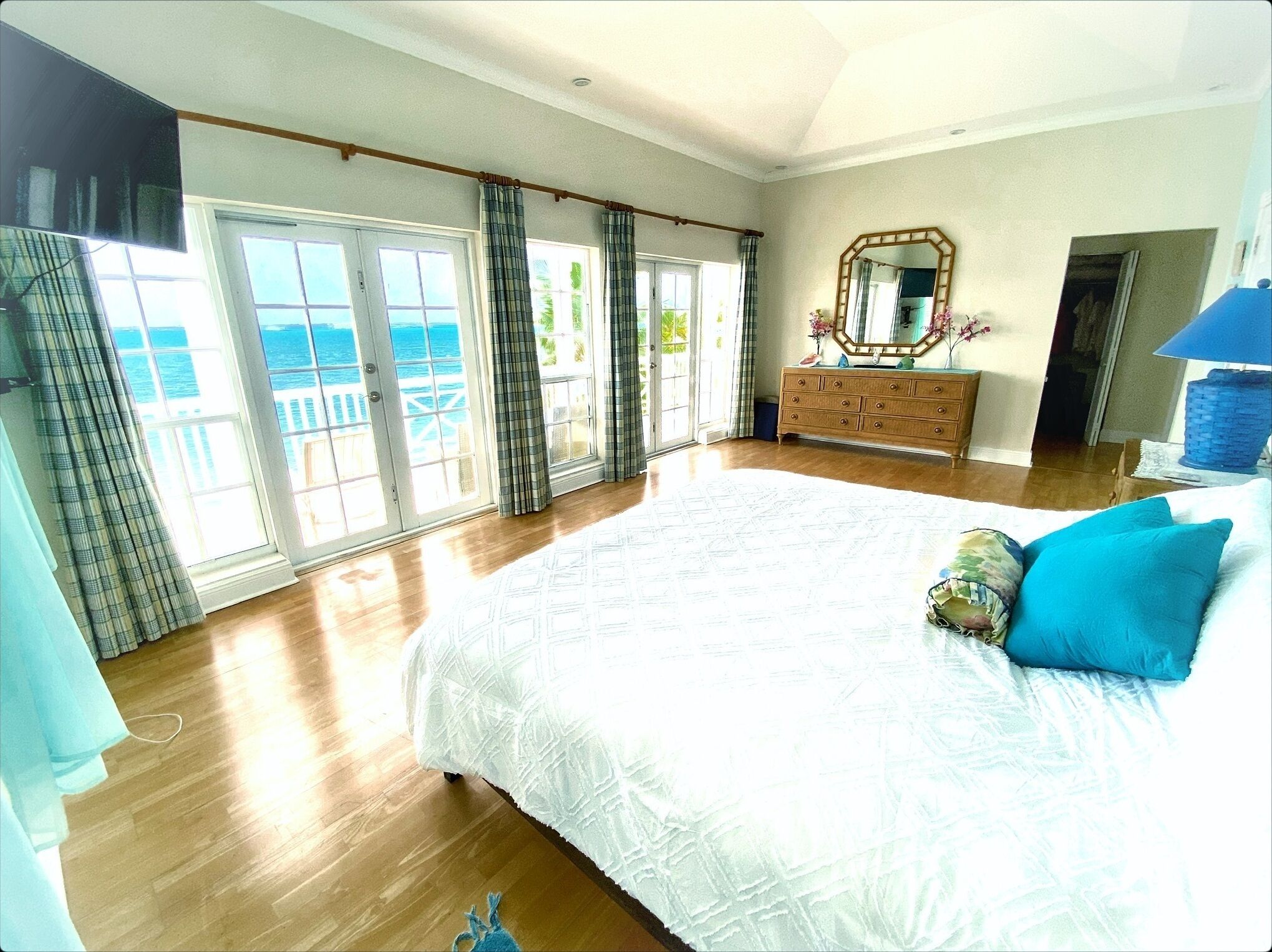 A bedroom with a large bed, a dresser, and a view of the sea through the windows.