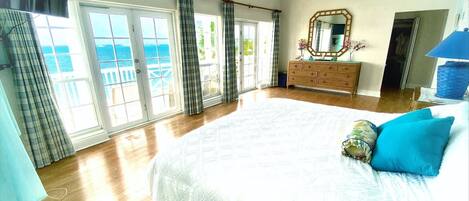 A bedroom with a large bed, a dresser, and a view of the sea through the windows.
