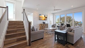 A spacious living area with a wooden staircase, a sofa, a coffee table, and a TV mounted on the wall.