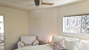 A bedroom with a bed, a chair, a nightstand, a ceiling fan, and a window with a view of trees.