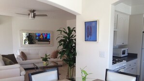 A modern living room with a glass dining table, a sofa, a TV, and a kitchen area with cabinets and appliances.