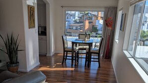 A spacious living area with a dining table and chairs, a sofa, and a large window with a view of buildings.