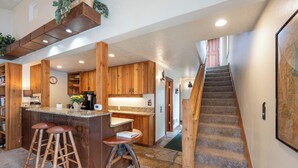 A kitchen with wooden cabinets, a bar area with stools, a staircase, and a dining area with a table and chairs. - Fresh interior, excellent location in Aspens (Wilson)