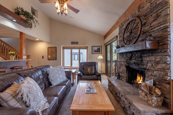 A cozy living room with a stone fireplace, leather sofa, and a wooden coffee table. - Fresh interior, excellent location in Aspens (Wilson)