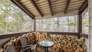 A covered outdoor seating area with chairs and a table, surrounded by stacked firewood. - Fresh interior, excellent location in Aspens (Wilson)