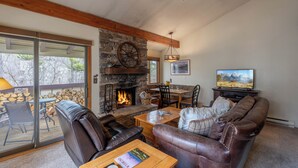 A cozy living room with a stone fireplace, leather sofas, a dining area, and a television. - Fresh interior, excellent location in Aspens (Wilson)