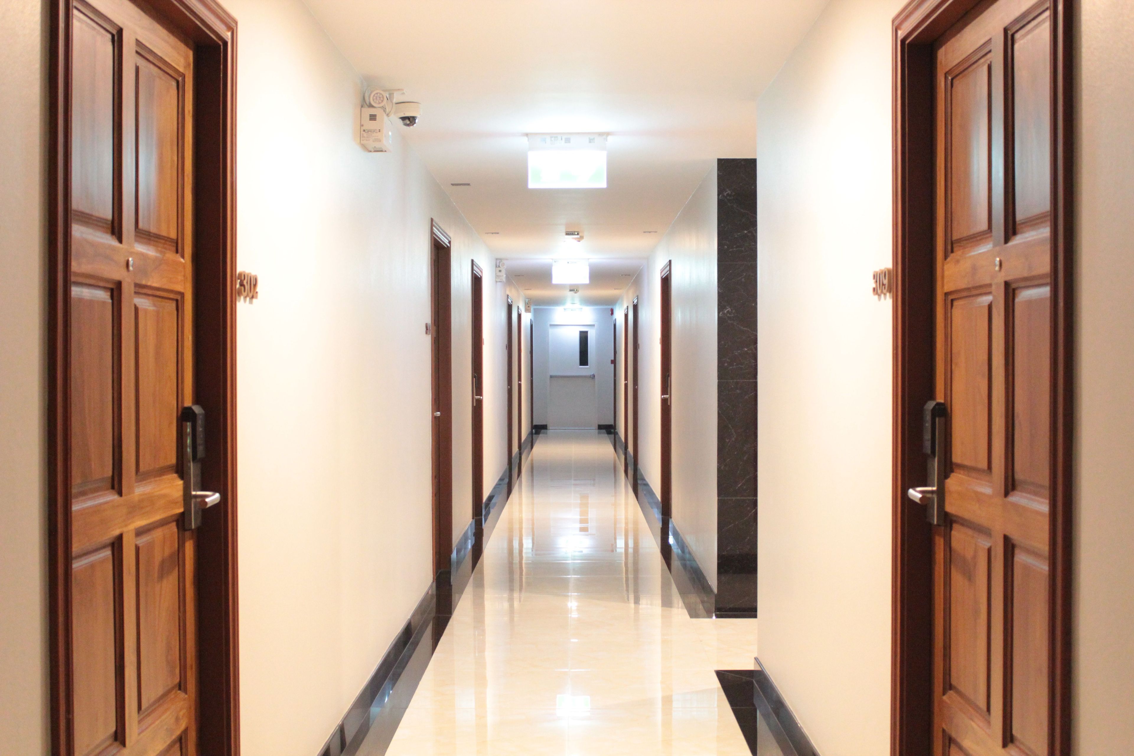 A hotel corridor with wooden doors, a marble floor, and a ceiling light.