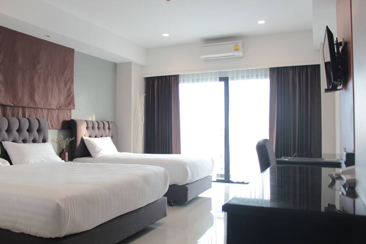 A hotel room with two beds, a desk, and a TV.