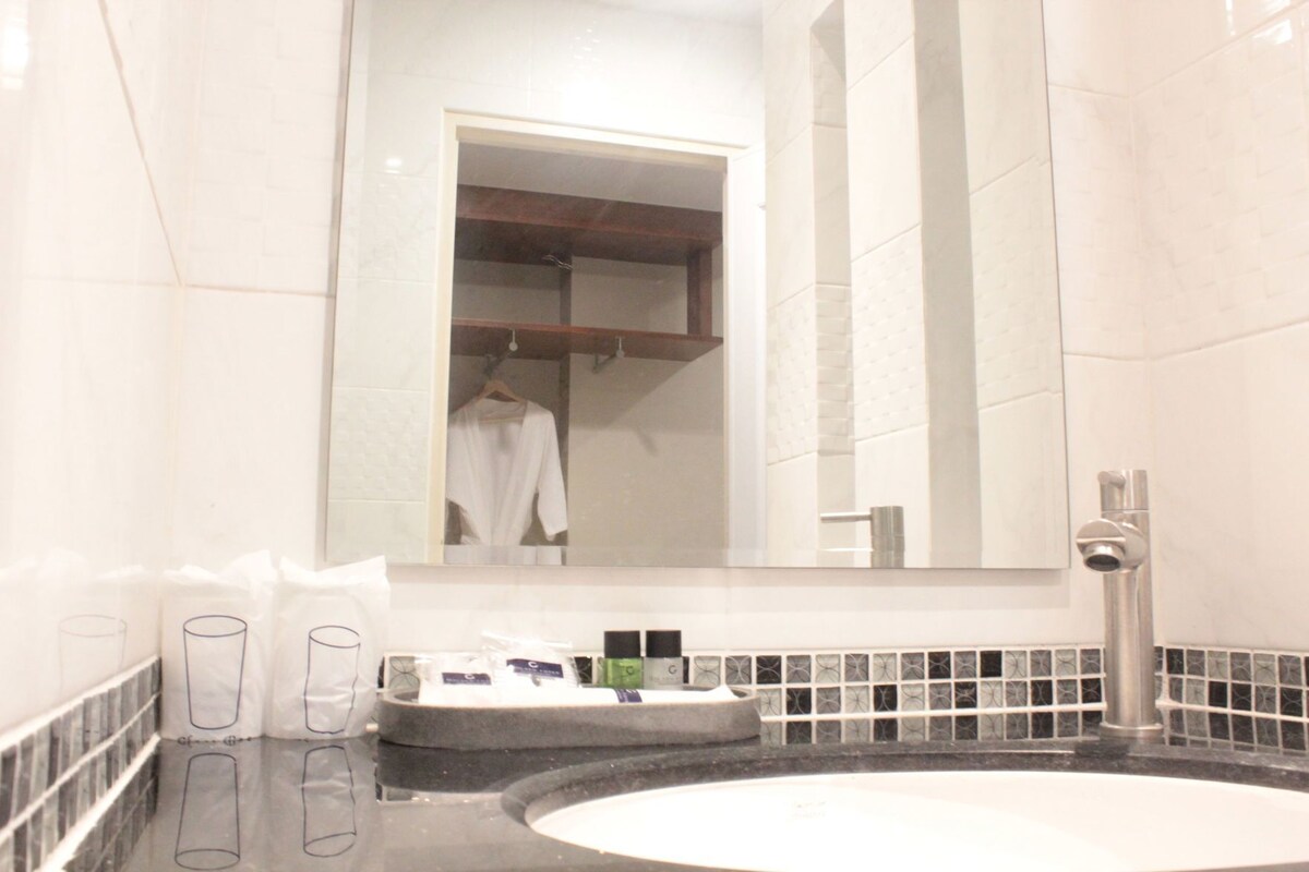 Un bagno con uno specchio grande, un lavandino con articoli da toilette e un accappatoio appeso allo specchio.