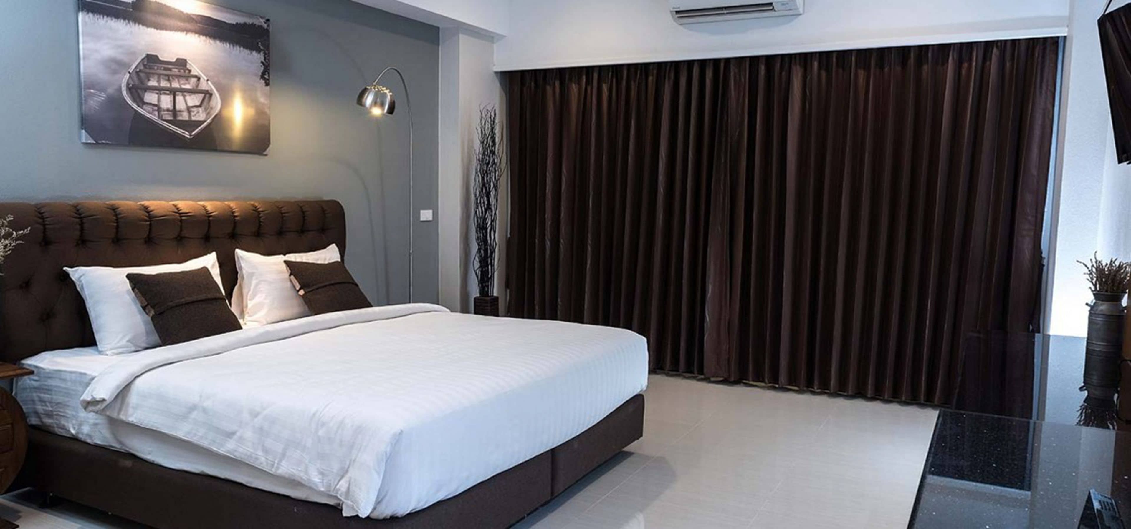 A modern bedroom with a large bed, a headboard, a wall-mounted air conditioner, and a window with dark curtains.