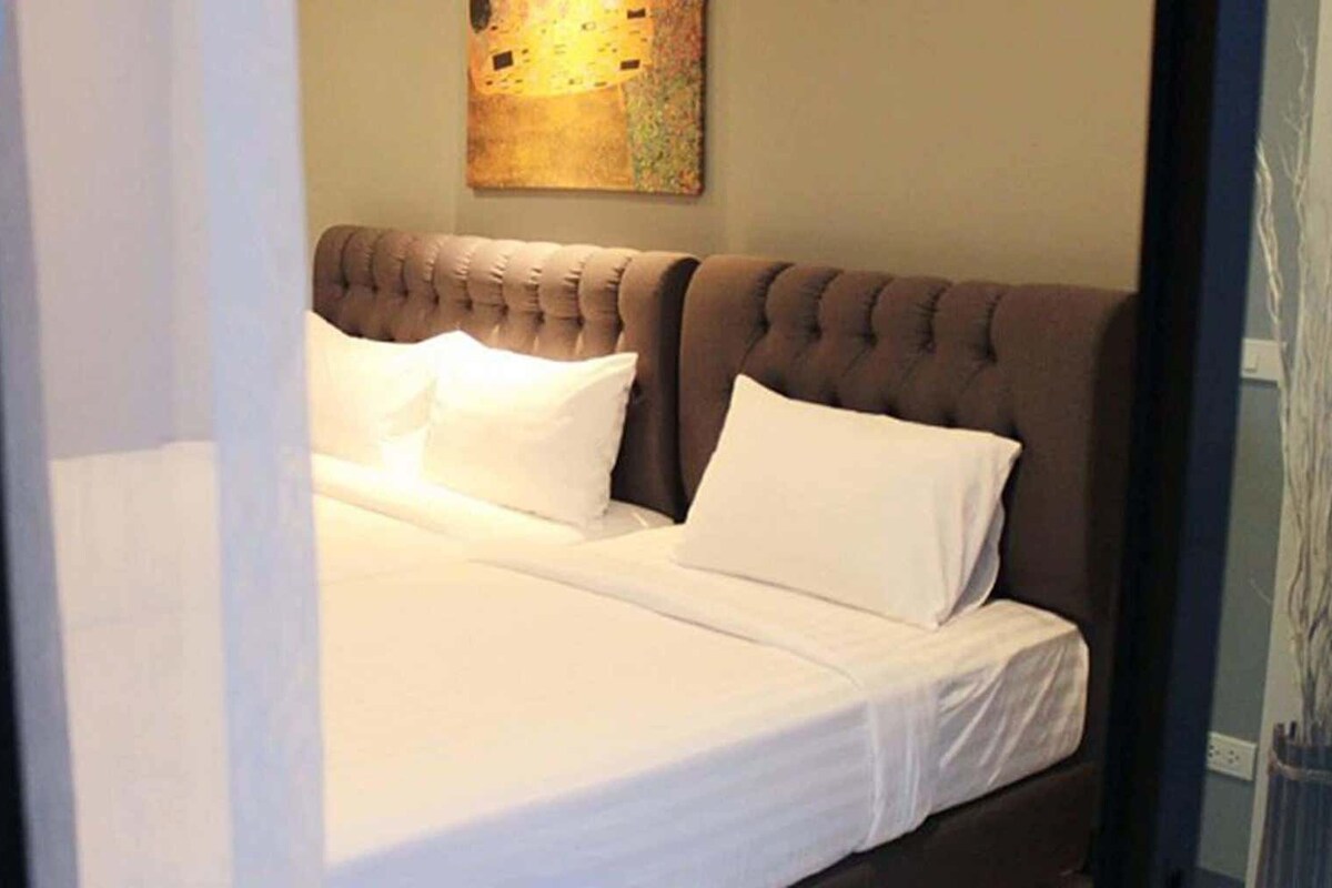 A neatly made bed with white linens and a tufted headboard in a hotel room.