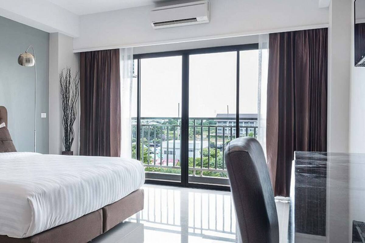 A modern hotel room with a large bed, a view of the city through the balcony, and a painting on the wall.