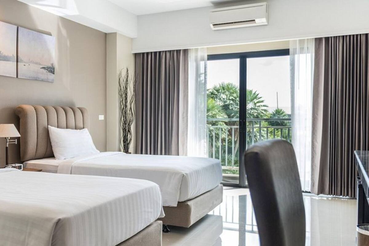 A hotel room with two beds, a desk, and a view of the outdoors.