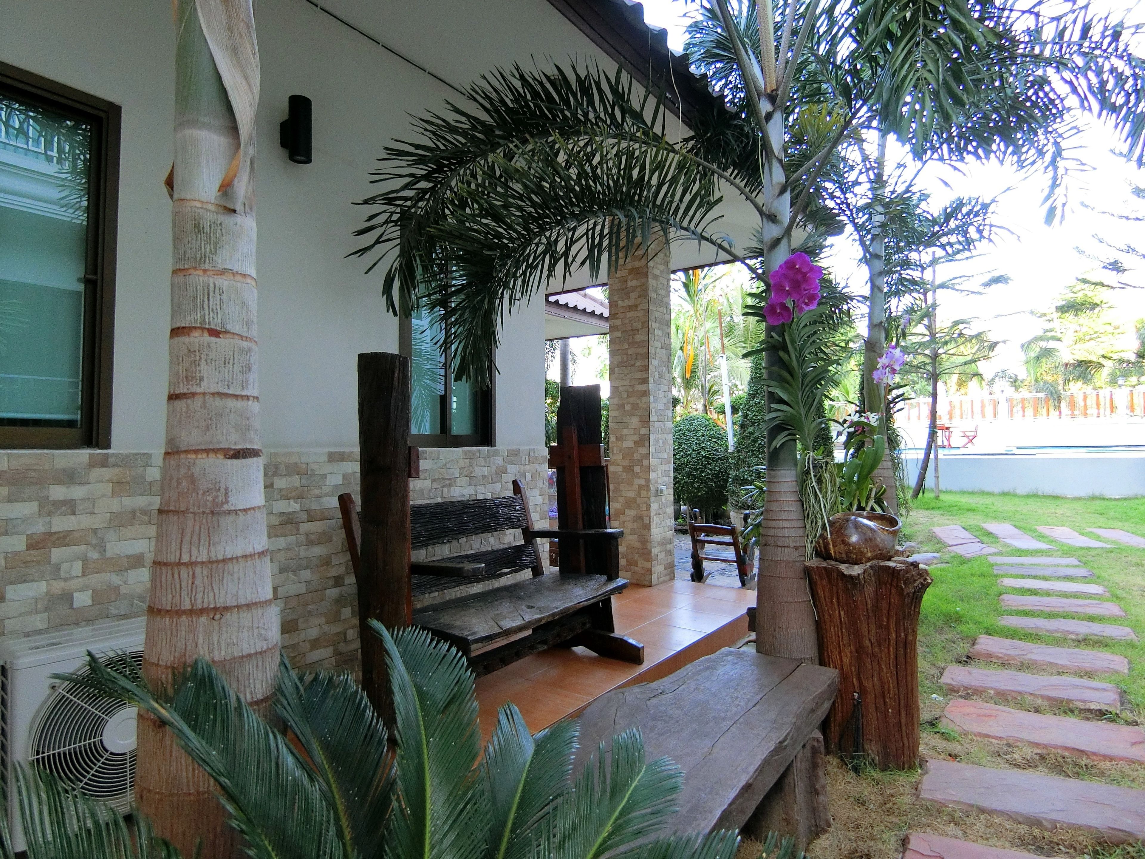 Un espacio al aire libre cubierto con un banco, rodeado de palmeras y una planta en maceta con flores moradas.