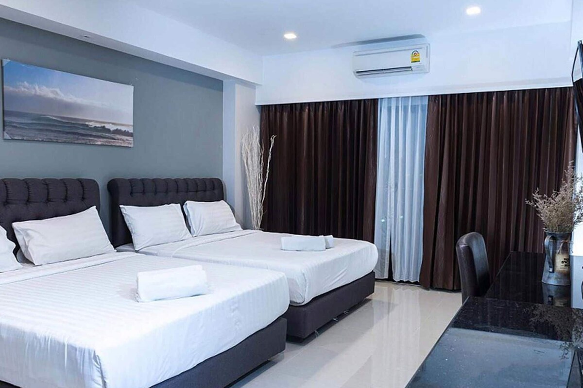 A hotel room with two beds, a desk, and a view of the ocean.