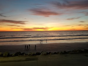 A sunset over the ocean with a beach and rocks in the foreground. - Incredible Ocean Views! Air Conditioning! Steps to the Sand! On The Strand (Oceanside)