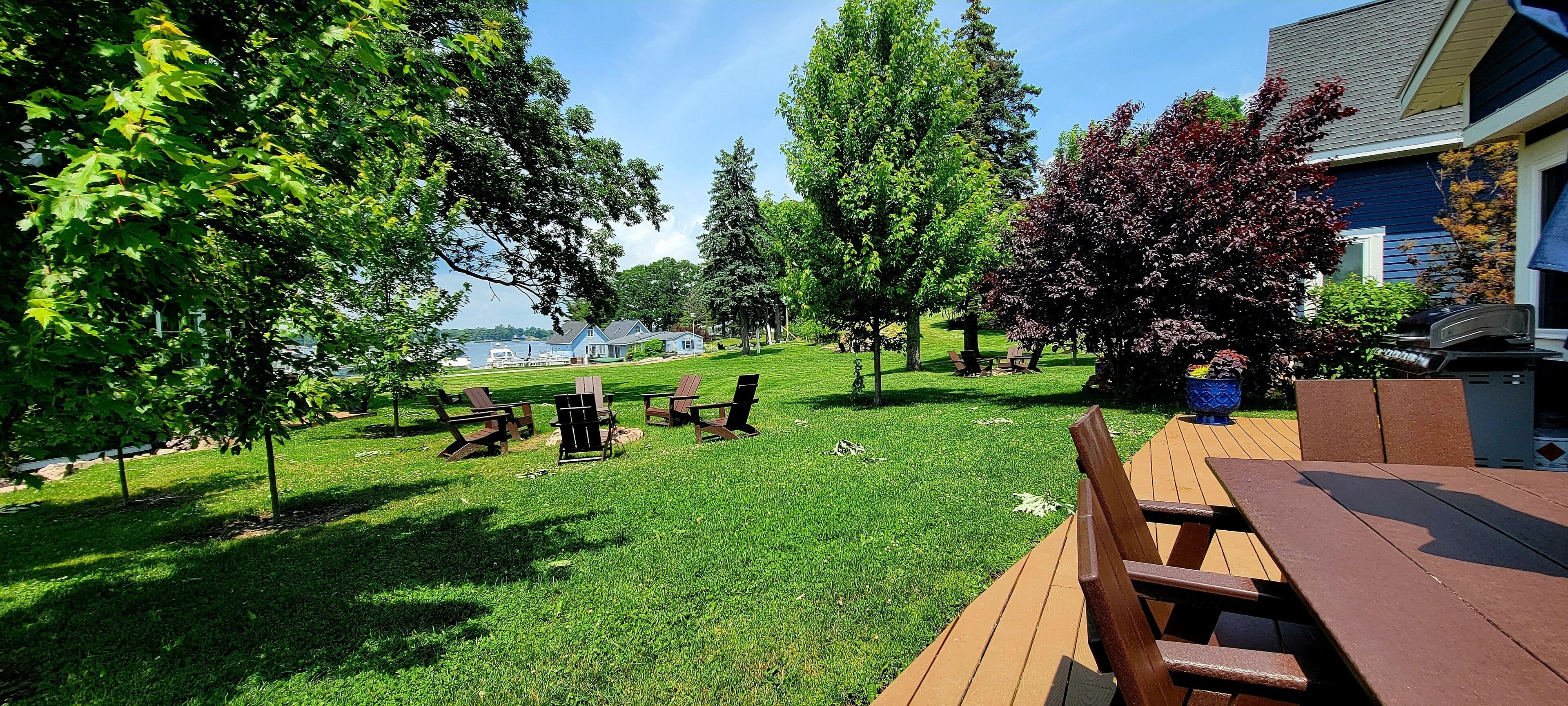 A backyard with a wooden deck, picnic tables, and a barbecue grill.