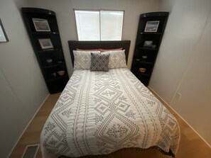 A bedroom with a bed, two nightstands, a window, and a wall-mounted shelf with decorative items.