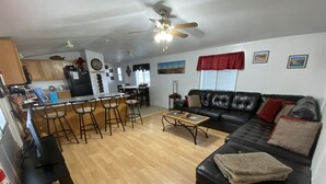 A modern living room with a black leather sofa, wooden coffee table, and a kitchen area with a bar counter and stools. - 50% to Book Home - Super Clean 3BR- Sleeps 6- By TNT (Page)