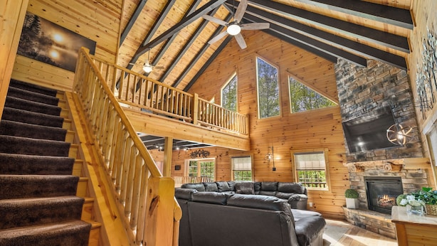 A spacious wooden cabin with a large living area, a fireplace, and a staircase leading to an upper level.