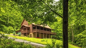 A log cabin with a porch, surrounded by lush green forest.