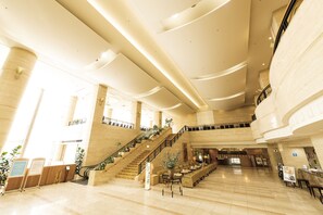 Un vestíbulo amplio con una imponente escalera, suelo de mármol y una zona de recepción.