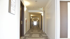 A hotel hallway with carpeted floors, doors on both sides, and wall-mounted light fixtures.