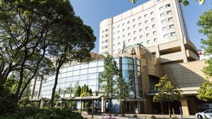 A modern hotel with a glass facade, a covered entrance, and a parking area.