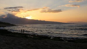 Eine Strandansicht mit Wellen, einem Sonnenuntergang und zwei Personen am Ufer.