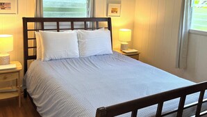 Ein ordentlich bezogenes Bett mit einem gemusterten Überwurf, zwei Nachttischlampen und einem Fenster mit Vorhängen.