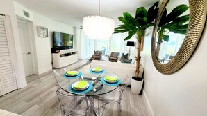 A modern dining area with a glass table, clear chairs, and a potted plant. - POSHPADZ-Bella Lago-Ground Floor, Walk to Jupiter Beach, Patio with Lake Views (Jupiter)