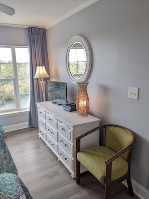 A room with a white dresser, a mirror, a lamp, and a chair.