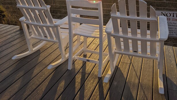 Dos sillas Adirondack en una terraza de madera con vista a una playa al atardecer.