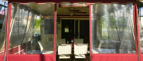 A covered outdoor seating area with a table and chairs, a ceiling fan, and a view of the water outside.