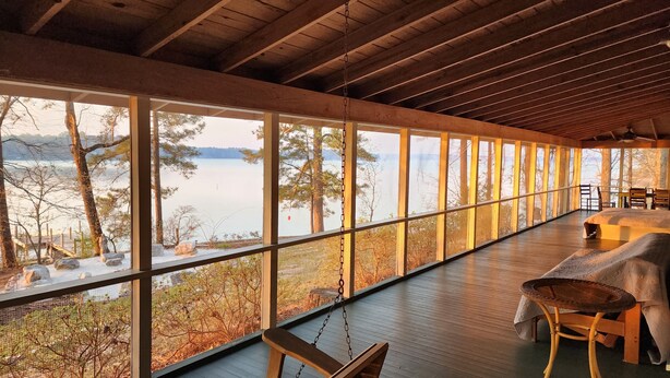 A cabin with large windows overlooking a lake, wooden deck, and a covered seating area. - Aubreys Lakewood Cabin -FREE DAY w Qualified Booking- Fishing, Football Friendly (Eclectic)