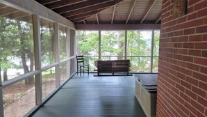 A covered porch with a bench and a chair, large windows, and a brick wall. - Aubreys Lakewood Cabin -FREE DAY w Qualified Booking- Fishing, Football Friendly (Eclectic)