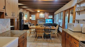 A cozy kitchen with wooden cabinets, a dining area with a table and chairs, a TV, and a stone fireplace. - Aubreys Lakewood Cabin -FREE DAY w Qualified Booking- Fishing, Football Friendly (Eclectic)