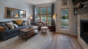 Una sala de estar acogedora con un sofá, un sillón y una mesa de centro, una chimenea y un ventanal con vistas a un lago.
