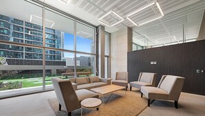 Un interior moderno con un sofá seccional, sillones y una mesa de centro. Ventanas amplias ofrecen vistas de la ciudad.