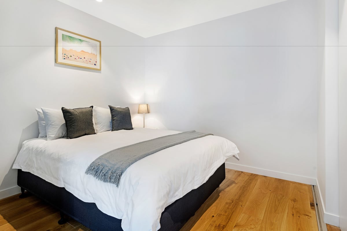 Une chambre à coucher avec un lit, des oreillers, une table de chevet, une lampe et un tableau encadré au mur.