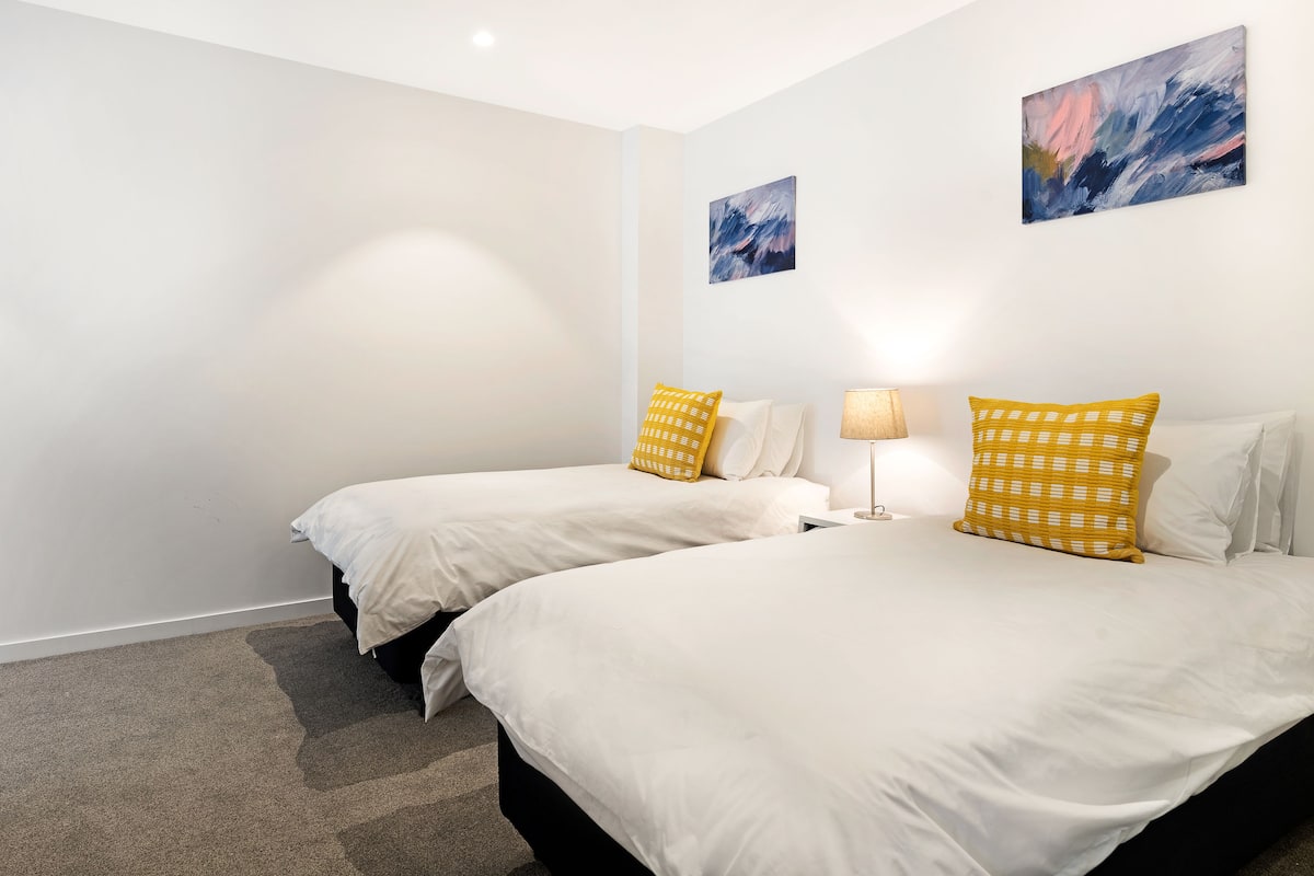 Une chambre d’hôtel avec deux lits, du linge de lit blanc et des oreillers à motifs jaunes.