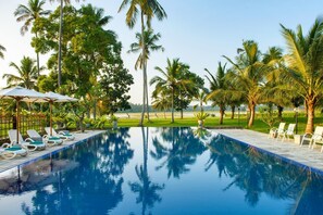 A swimming pool with lounge chairs and umbrellas, surrounded by palm trees and a grassy area. - The Notary's House (Pannala)