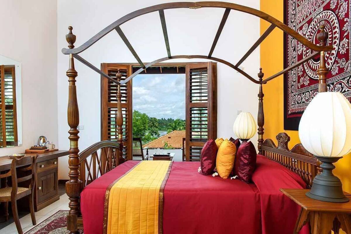 Een bed met houten hoofdbord, een rode sprei en twee lampen.