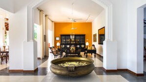 A spacious living area with a large decorative bowl in the center, a ceiling fan, and a black cabinet with framed pictures. - The Notary's House (Pannala)
