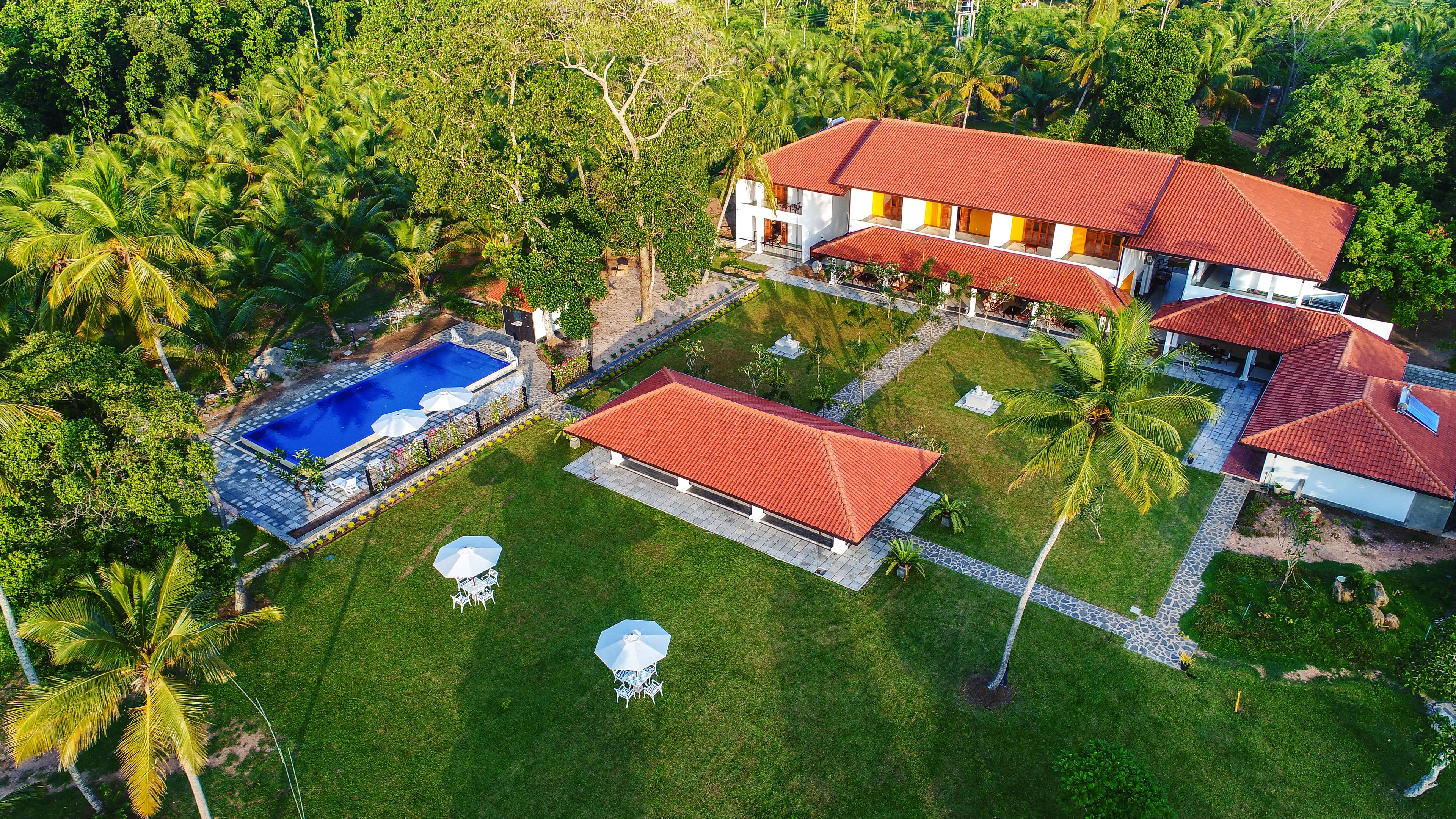 Vista aérea de um resort com piscina, vários edifícios com telhados vermelhos e vegetação exuberante.