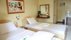 A hotel room with two single beds, a bedside table, a wall-mounted mirror, a small shelf with decorative items, and a trash bin. - Danel Pensionne House (Tacloban)