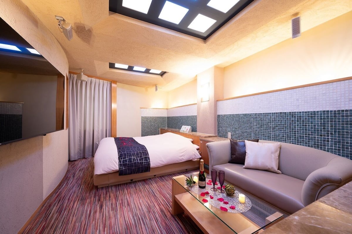 A hotel room with a bed, a sofa, a glass coffee table, and a tiled wall.