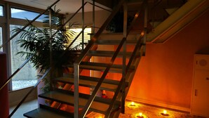 Una escalera con barandillas metálicas, una planta en maceta y una vela encendida en el suelo.