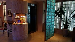 Un vestíbulo con un expositor iluminado de forma circular, un área de descanso con una mesa y una planta grande en maceta.